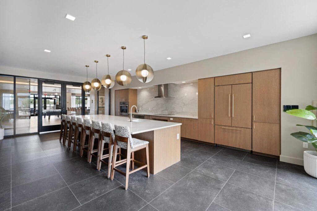 Sleek communal kitchen with an island, barstools, hanging globe lights, and wood cabinetry in a modern open layout.