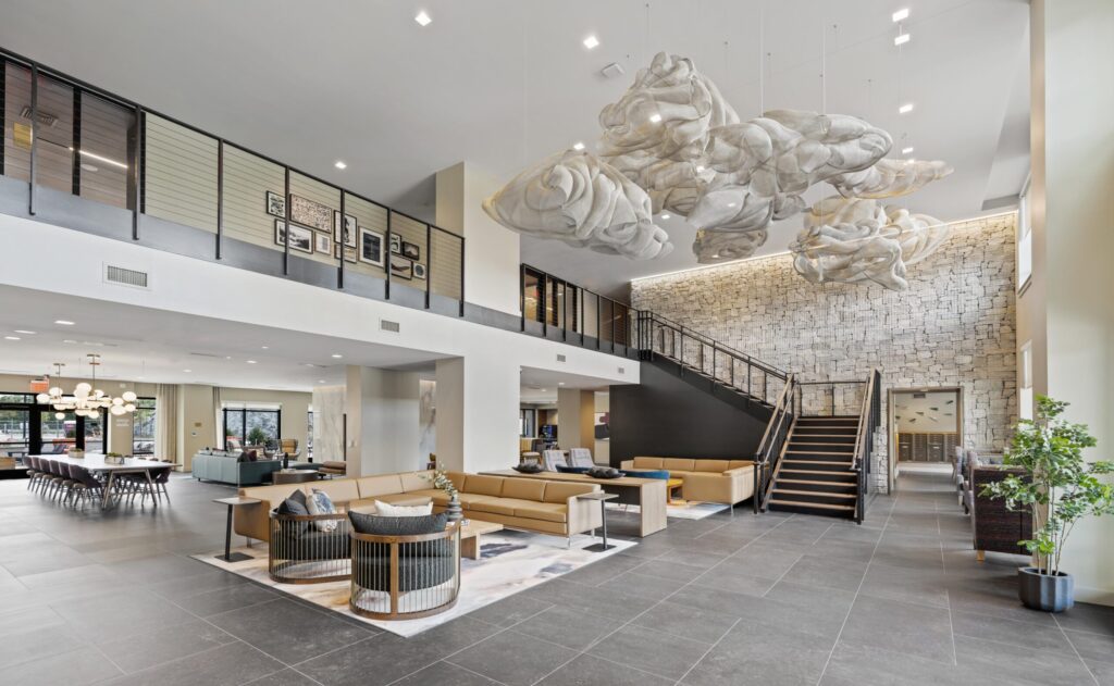 Expansive lobby with seating areas, floating cloud-like sculptures, a stone accent wall, and a staircase leading to the upper level.