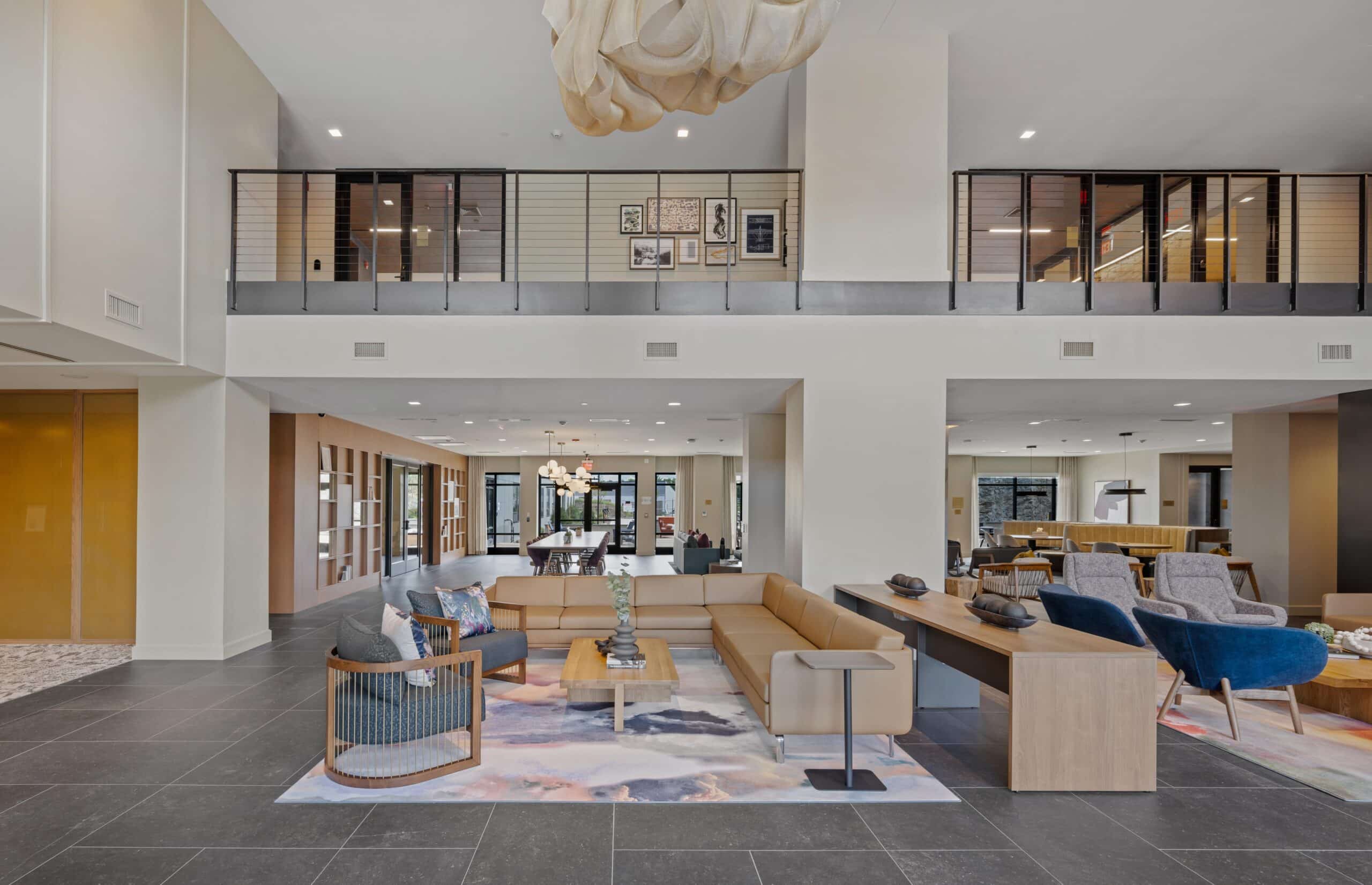 Contemporary lounge area with beige and blue seating, decorative rugs, and open views of a two-story space with wall art.