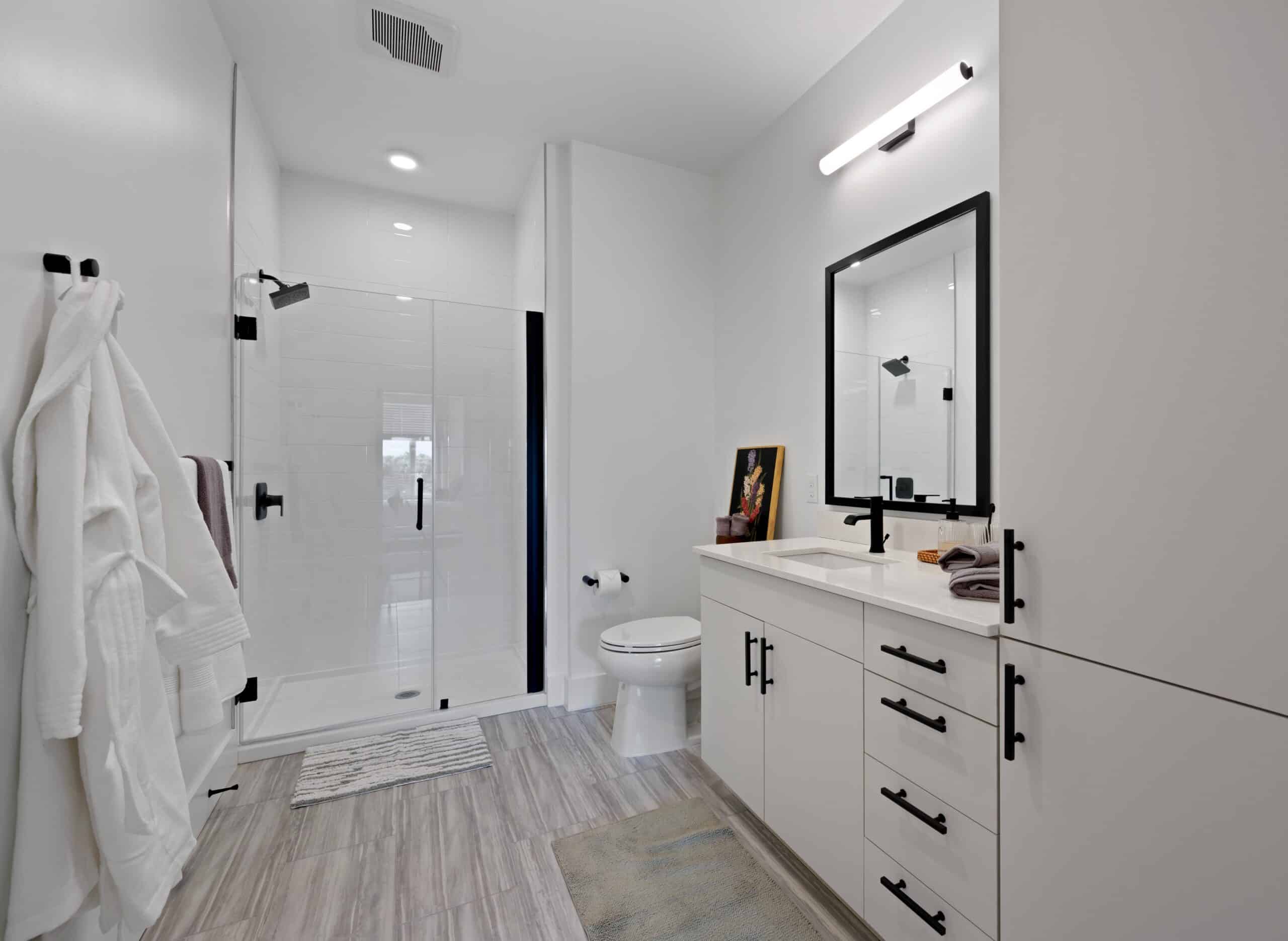 Modern bathroom with a glass shower, double sink vanity, large mirror, and clean white decor with black accents.