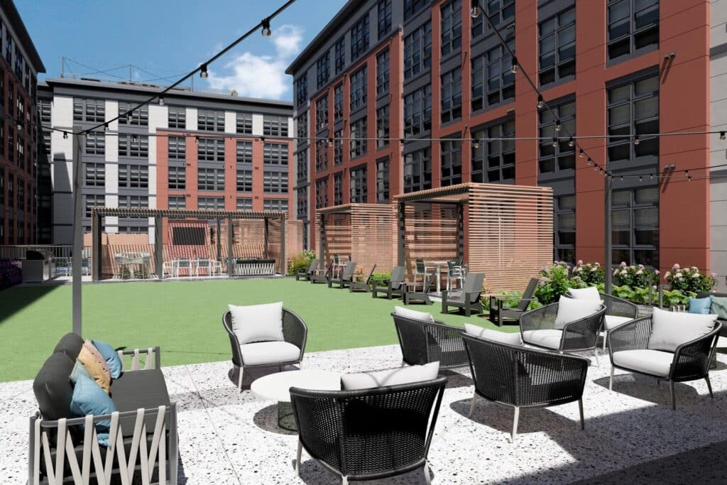 Outdoor lounge area with wicker seating, string lights, and shaded cabanas, surrounded by modern apartment buildings.