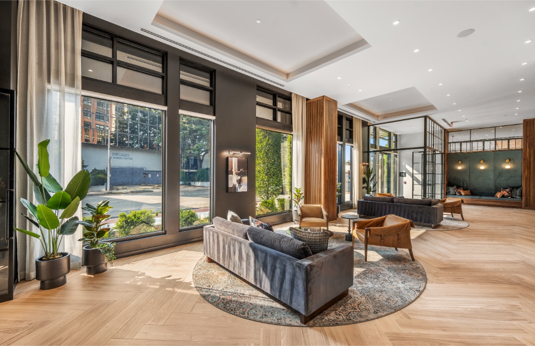 Elegant lobby with high ceilings, floor-to-ceiling windows, blue and tan seating, and wood accents on the walls and floors.