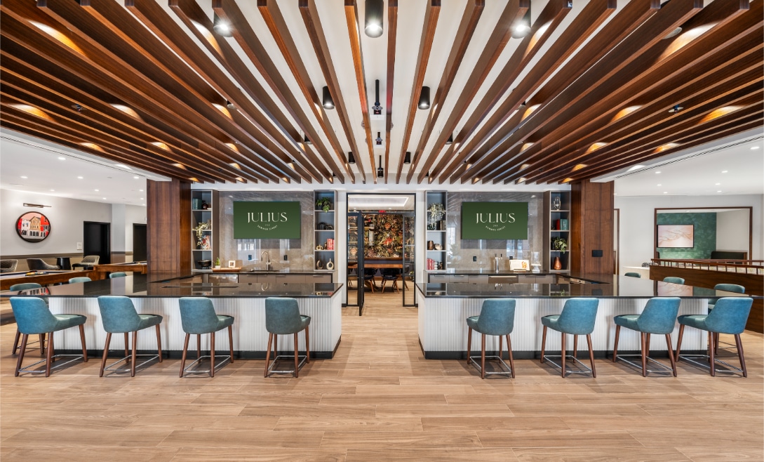 Chic bar area named "Julius" with teal bar stools, wood ceiling panels, and two symmetrical serving counters.