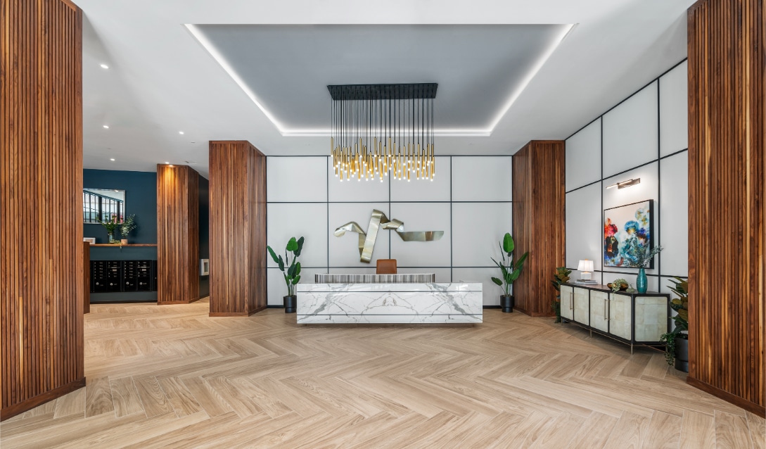 Elegant lobby with a marble reception desk, wood accents, abstract art, and a striking gold pendant light fixture.