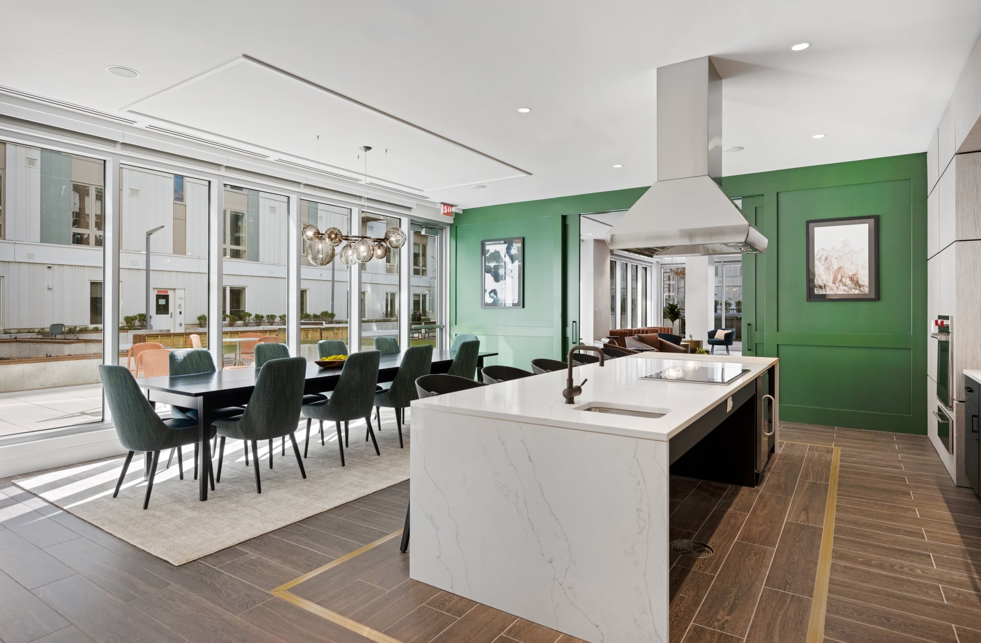 Elegant room with a large white island, green dining chairs, and glass pendant lighting, opening to a bright outdoor space