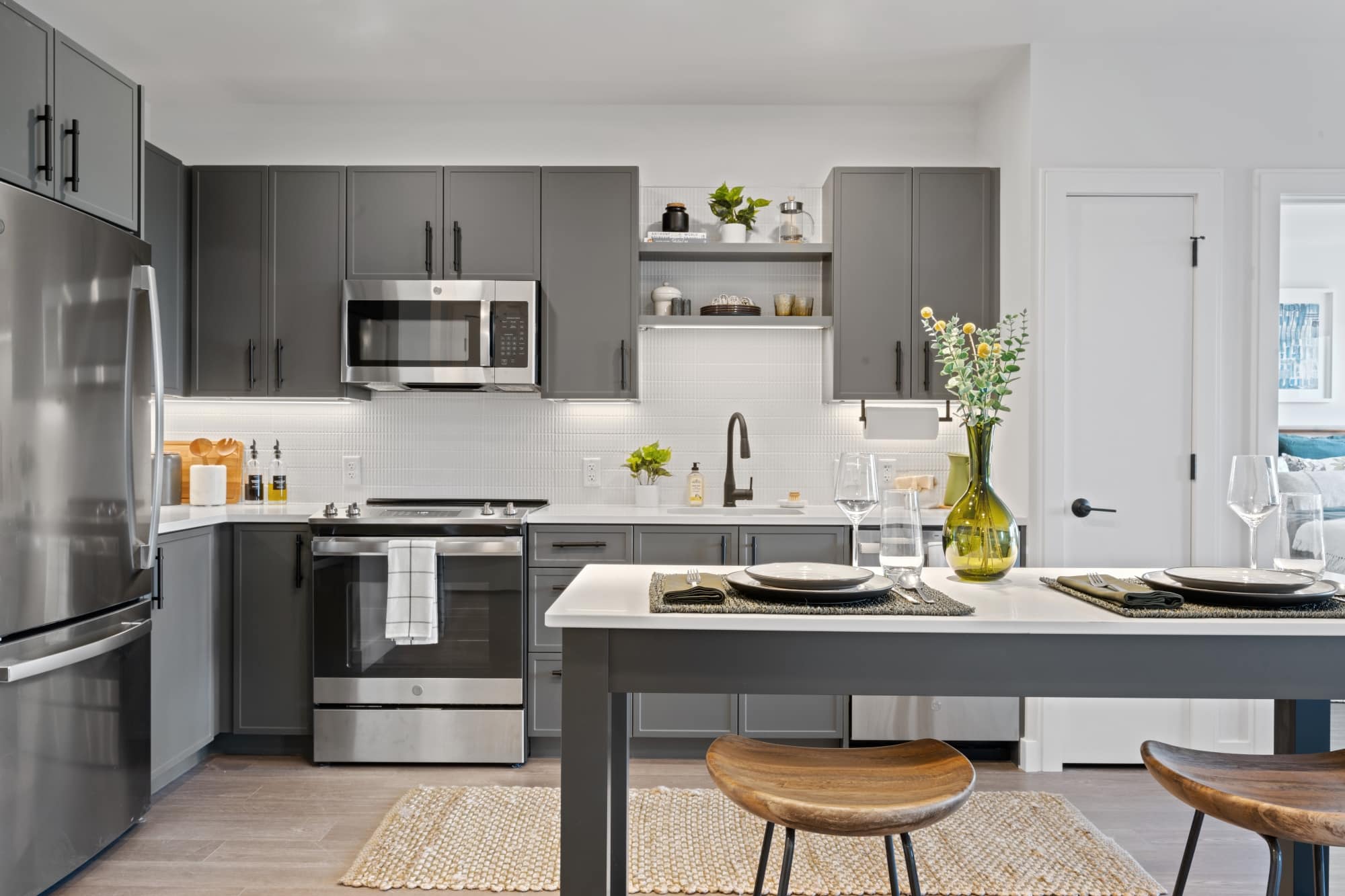 Modern kitchen with dark gray cabinets, stainless steel appliances, and a dining island set with plates and a vase of flowers.