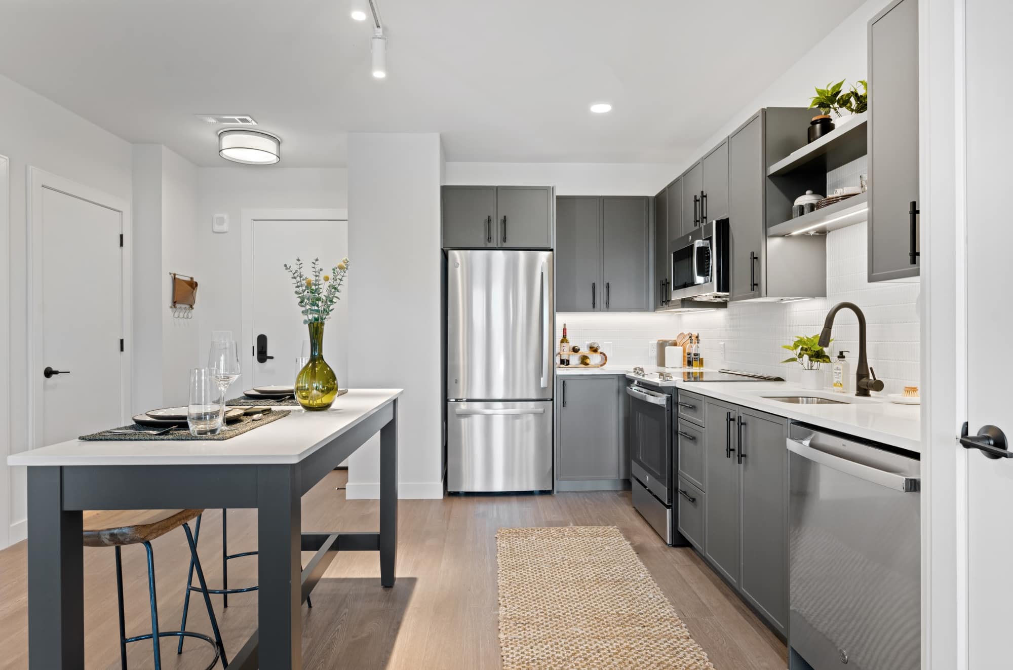 Modern kitchen with gray cabinetry, stainless steel appliances, and a dining island with minimalist table settings and a green vase.