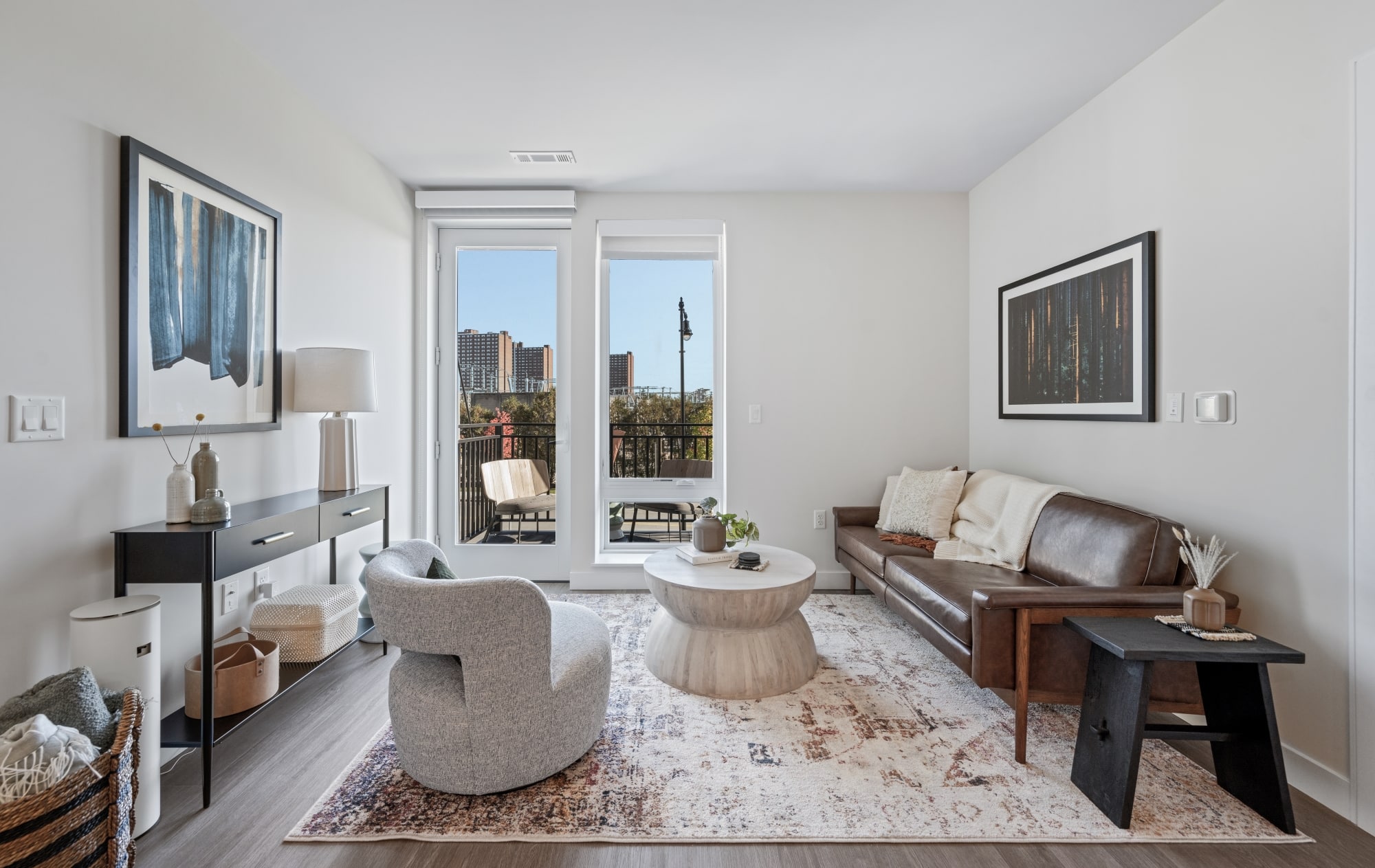 Bright living room with a leather sofa, abstract art, and access to a balcony with a view of the city skyline.