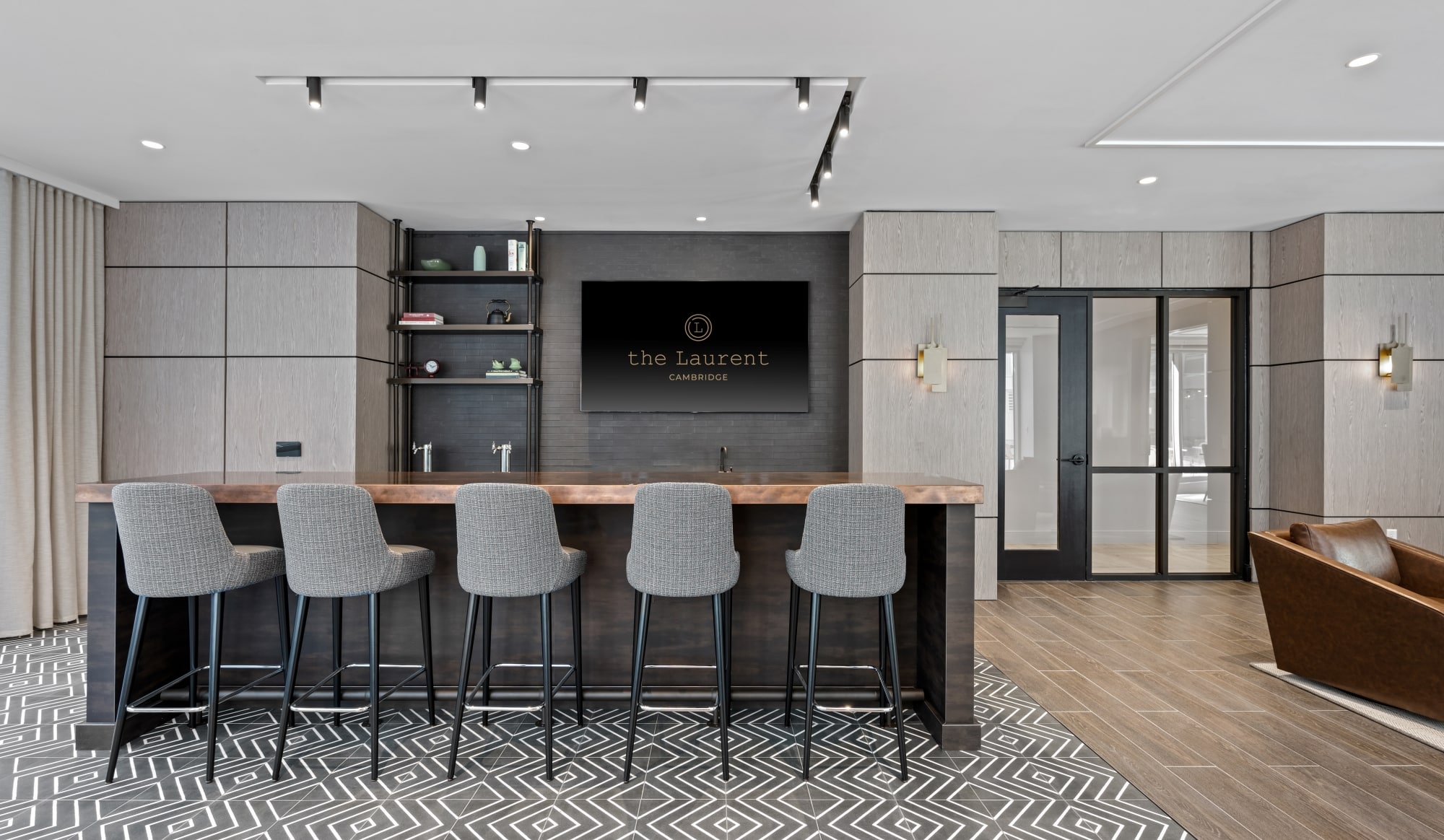 Lounge bar area with upholstered high stools, a wooden countertop, and a large display reading "The Laurent Cambridge."