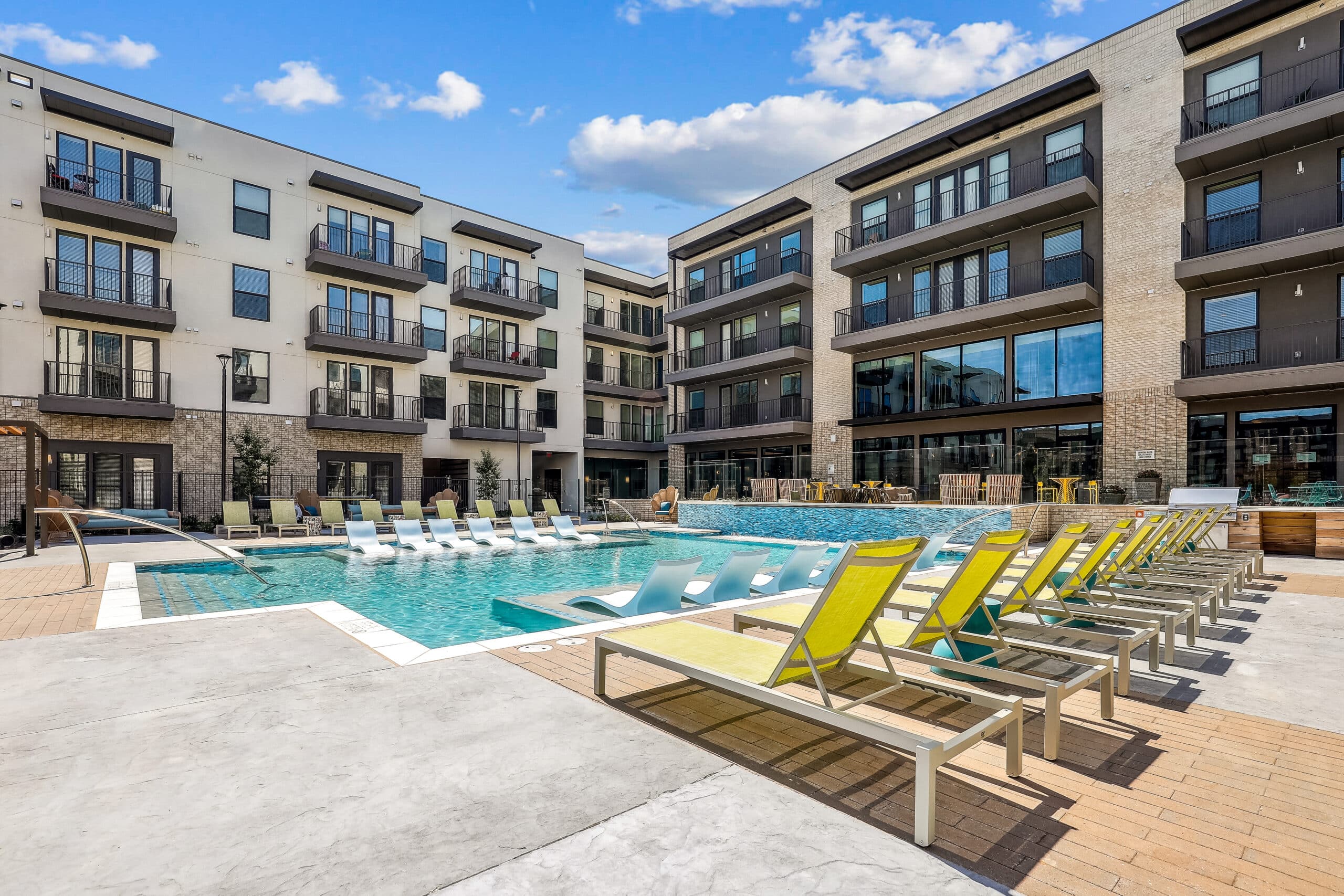 Apartments with balconies overlooking an outdoor courtyard with pool and yellow lounge chairs