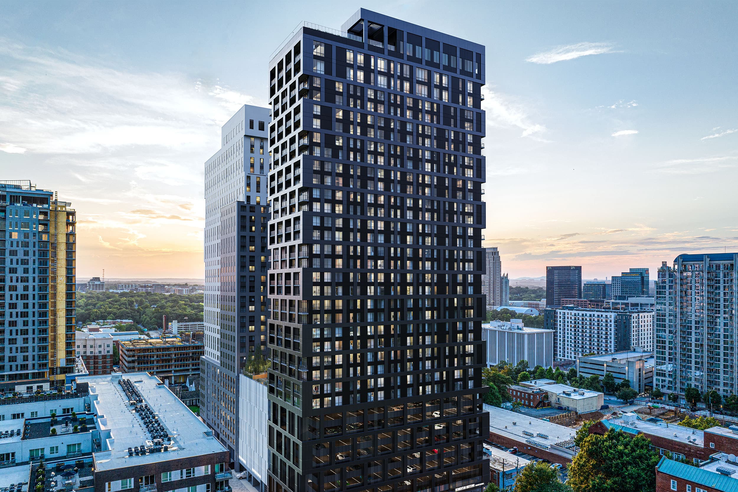 Exterior photo of a high-rise apartment building surrounded by other buildings with the sunset in the background.